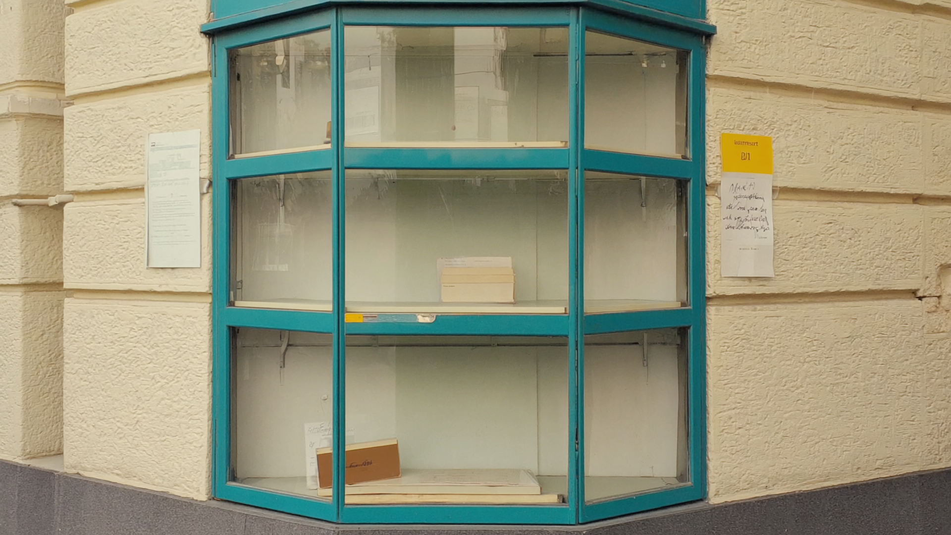 Öffentlicher Bücherschrank an einer Straßenecke, halb gefüllt mit gebrauchten Büchern, Glas leicht beschlagen